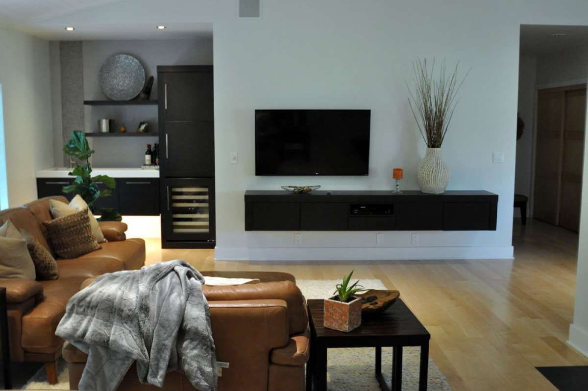 Modern living room with tan sofa, black TV console, coffee table, and open shelving