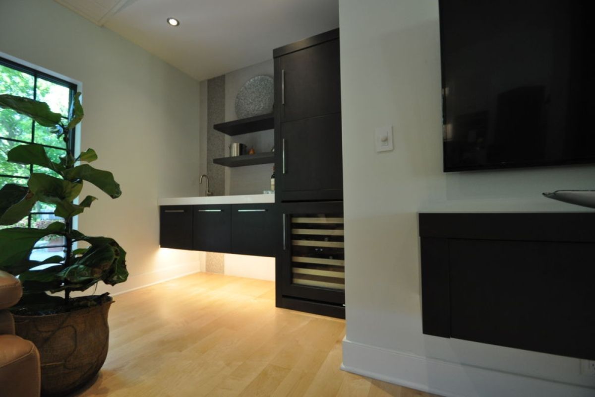 Modern living room with built-in kitchen, dark cabinets, wood floors, large window, and wall-mounted TV