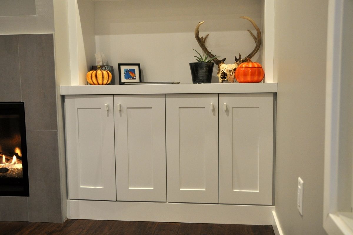 White cabinet with fall decor, pumpkins, framed photo, and potted plant in a living room alcove