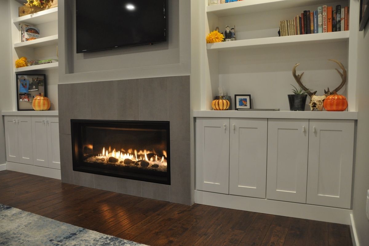 Living room fireplace with built-in white shelves and cabinets, TV above, and dark hardwood floors