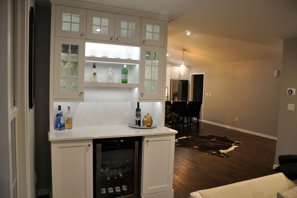 Home bar cabinet with white cabinets and glass shelves in a living room, adjacent to a dining area.