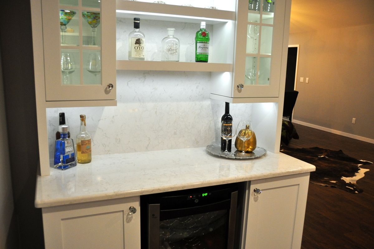 Built-in bar cabinet with glass shelves, liquor bottles, and white marble countertop in a living room