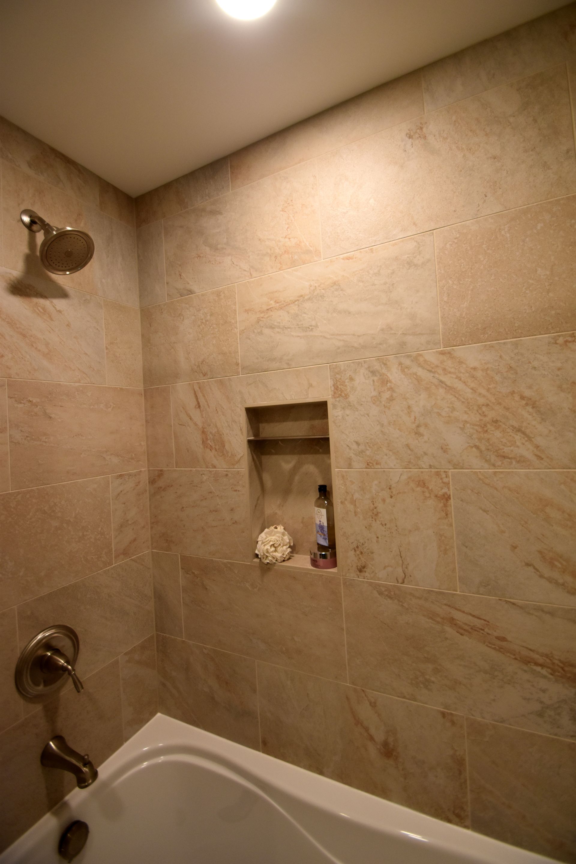 Stone-tiled shower with a built-in niche above a bathtub, lit by a ceiling light.