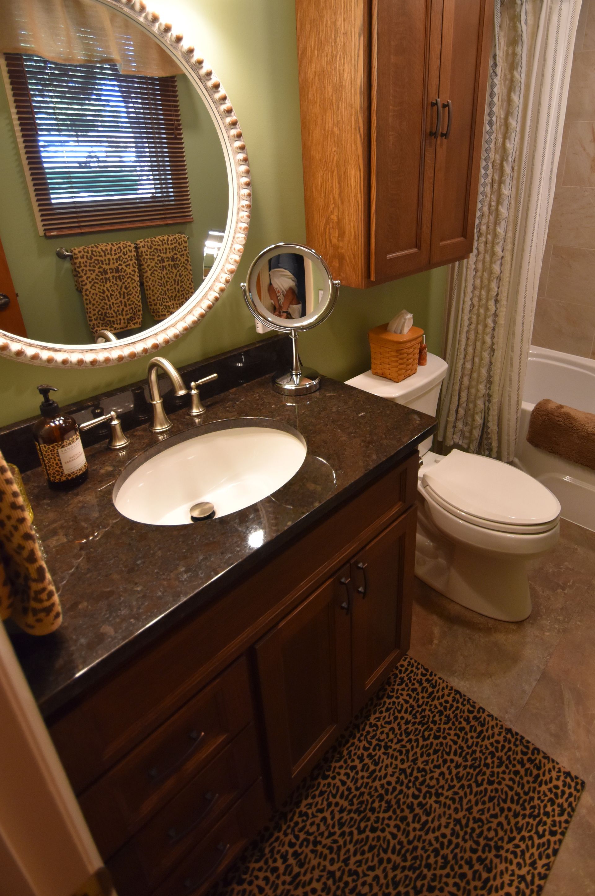 Bathroom with dark wood vanity, round mirror, sink, toilet, and leopard-print rug.