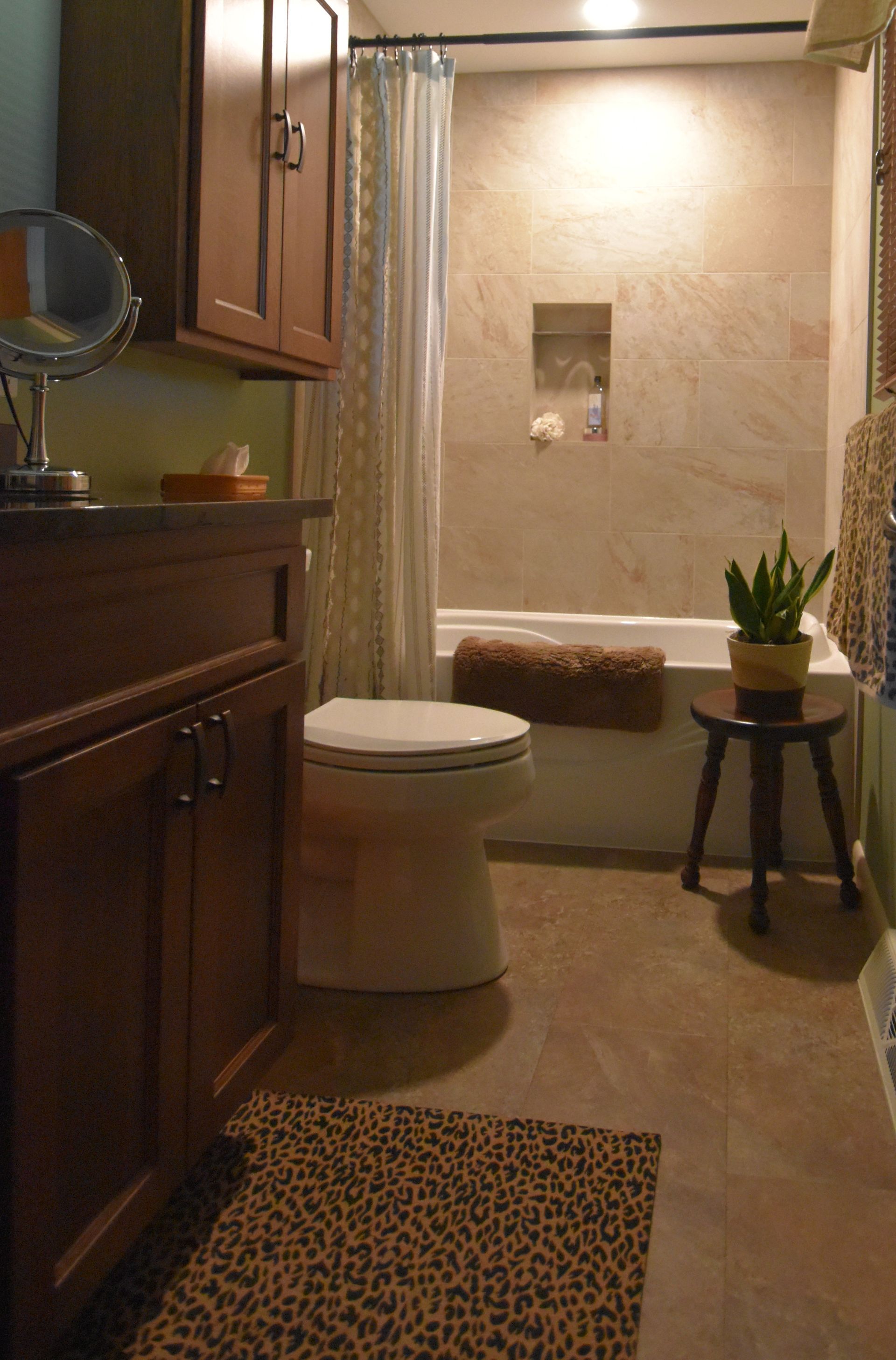 Small bathroom with toilet, tub shower, dark wood vanity, and a leopard-print rug