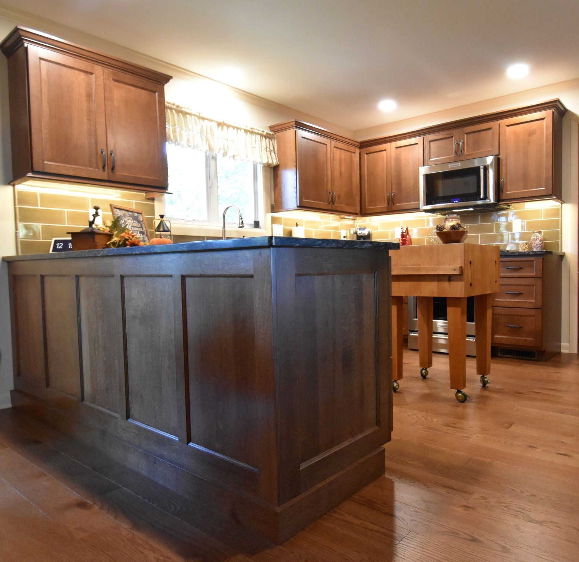 Modern kitchen with dark wood cabinets, island, hardwood floors, and a small dining table by the window