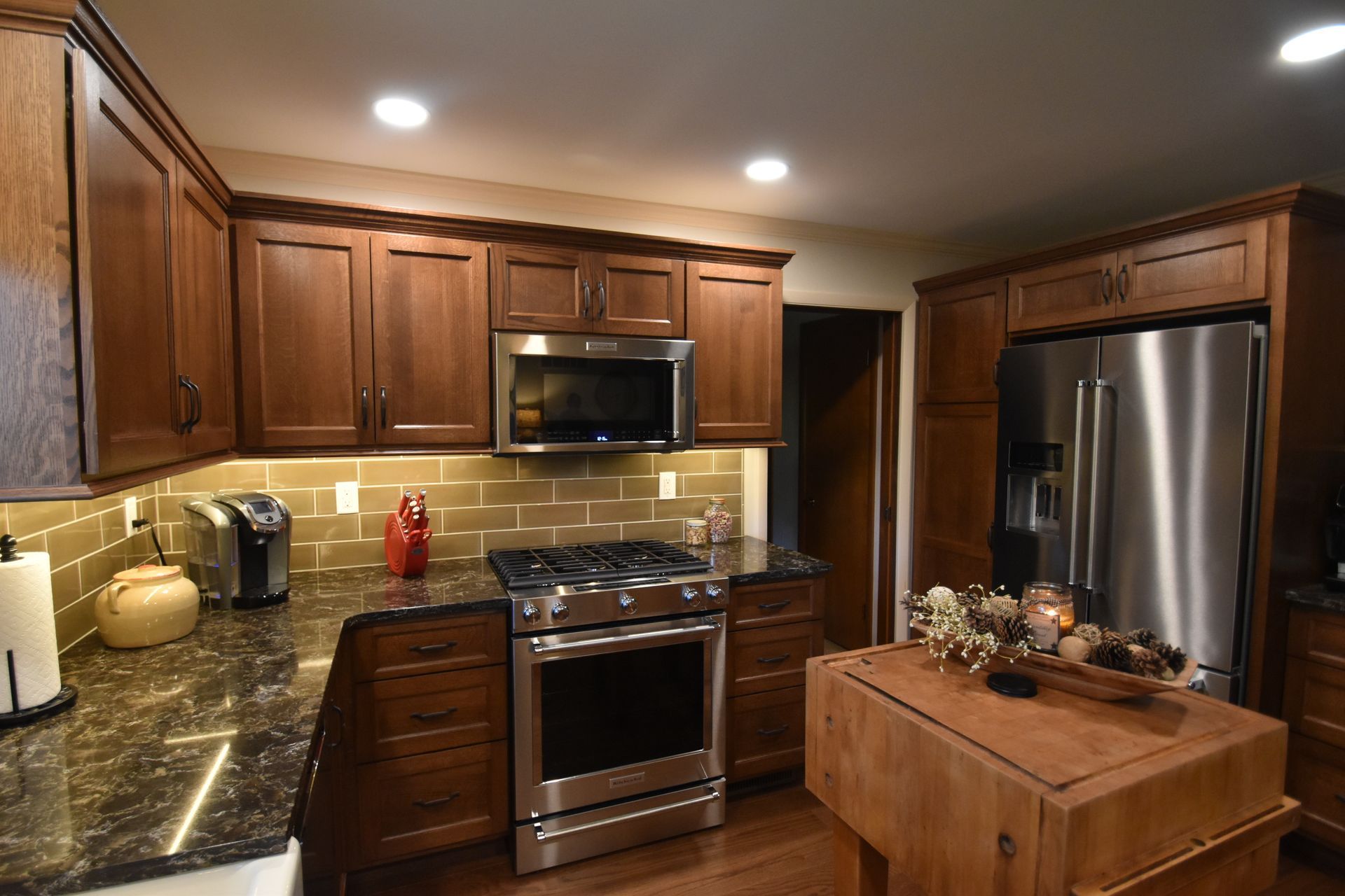Warm wood kitchen with stainless steel appliances, granite counters, and a small island centerpiece.