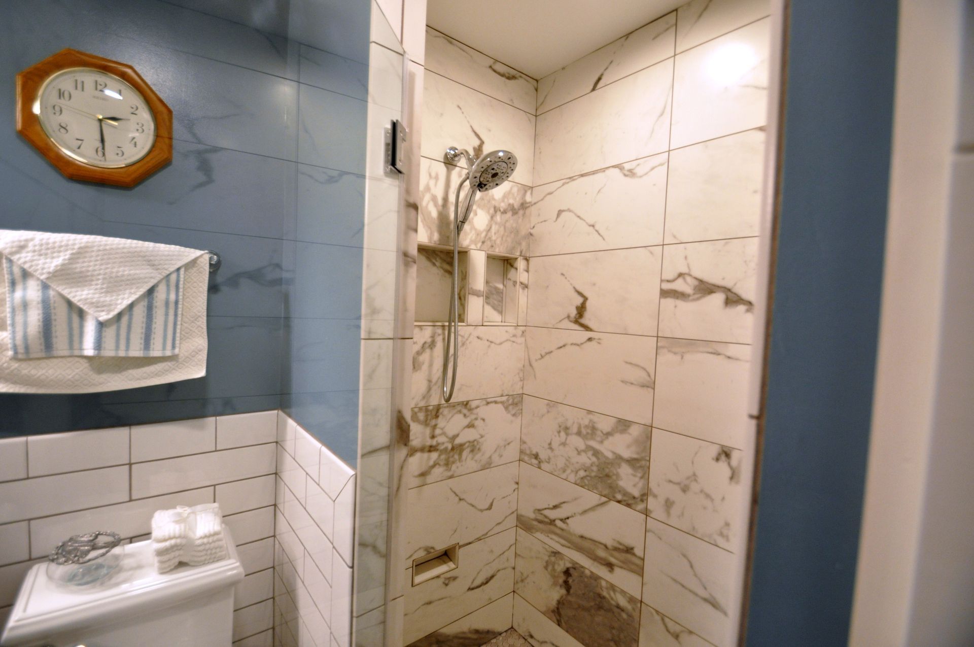 Compact bathroom with blue and white tiled shower, towel rack, and wall clock