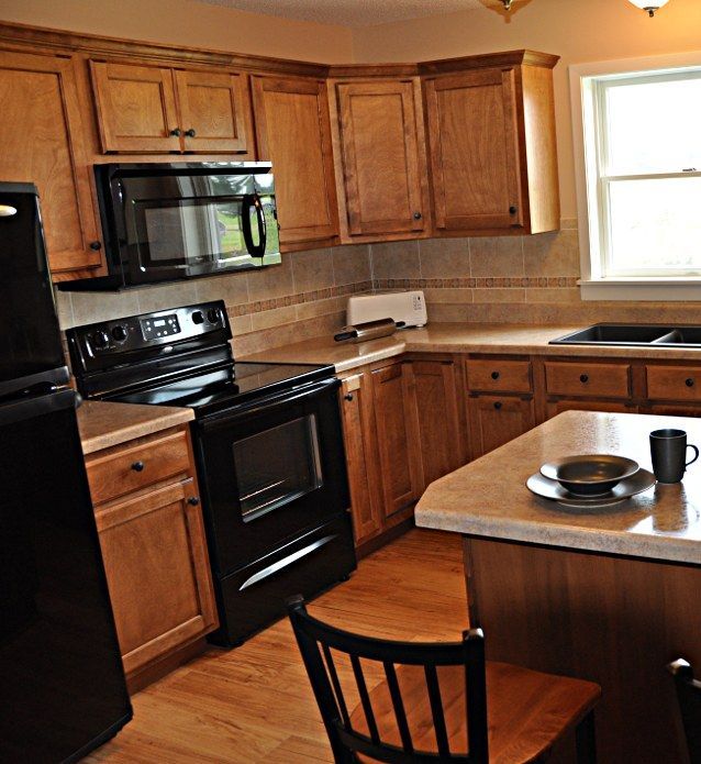 Small kitchen with wooden cabinets, black appliances, and a counter table with plates and mugs.