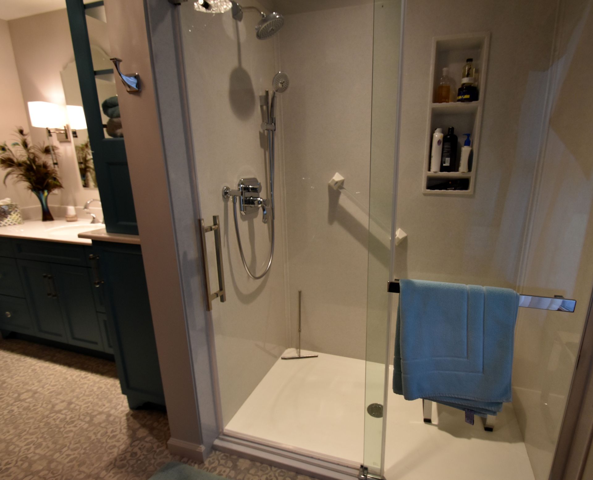 Walk-in shower with glass doors, chrome showerhead, and a blue towel in a modern bathroom.