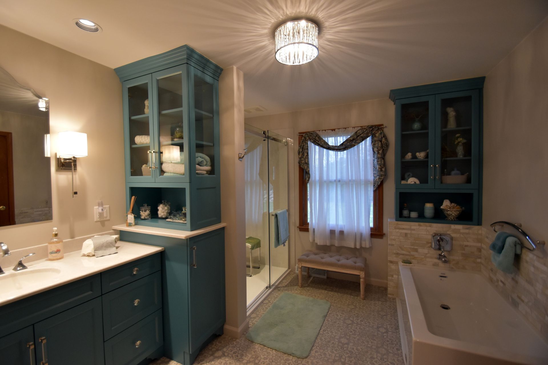 Bright bathroom with teal cabinets, a clawfoot tub, vanity, and window seat by a curtained window.