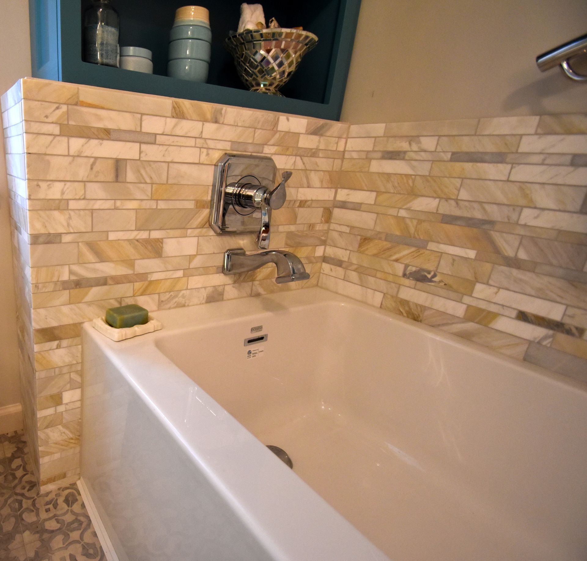 Corner bathtub with beige tile surround, wall-mounted faucet, and shelf of toiletries in a bathroom.