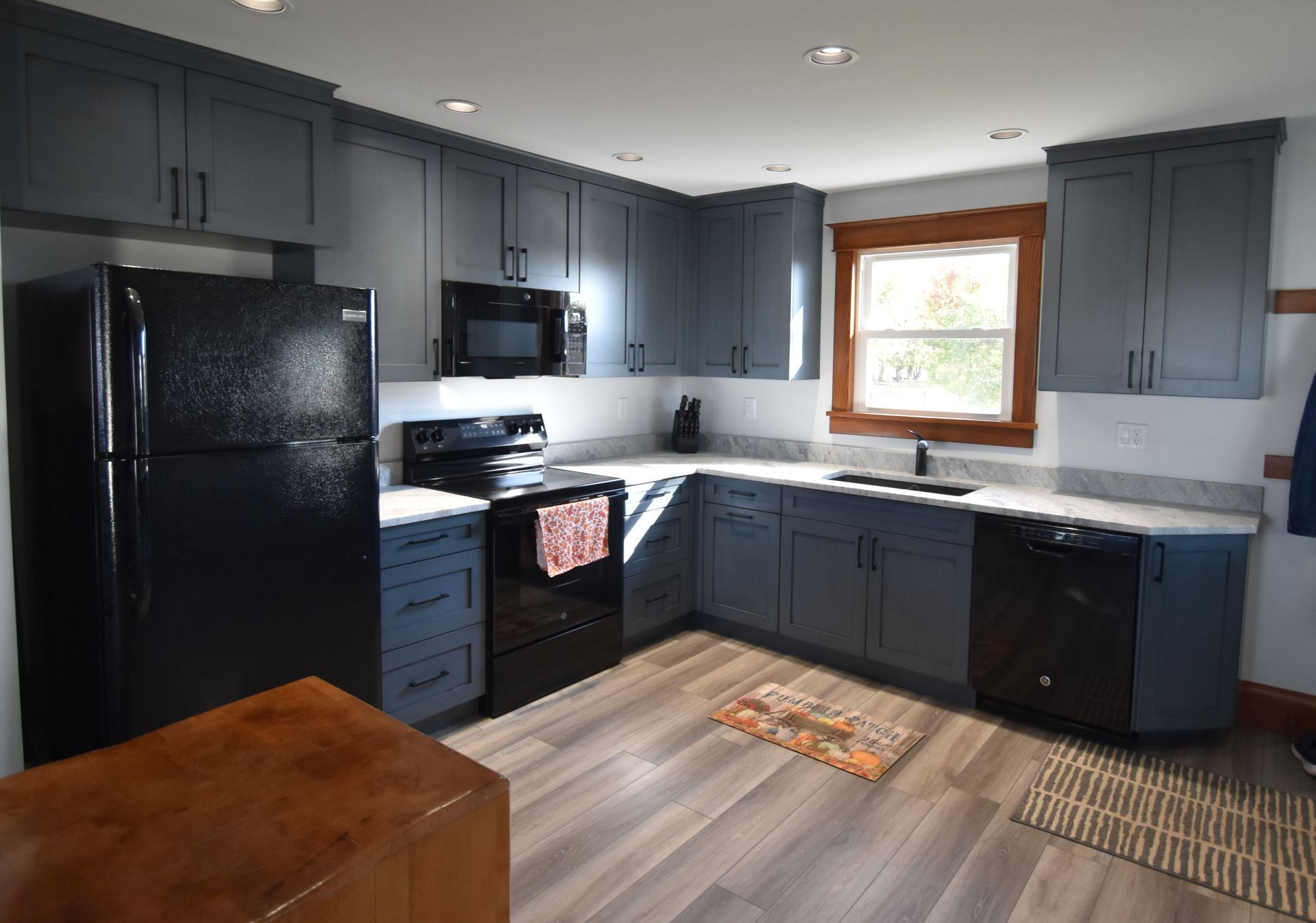 Modern kitchen with dark cabinets, black appliances, white countertops, and a window over the sink