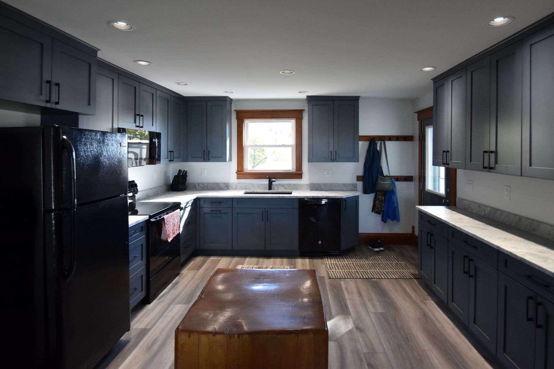 Modern kitchen with dark cabinets, black appliances, wood floor, and a window over the sink.
