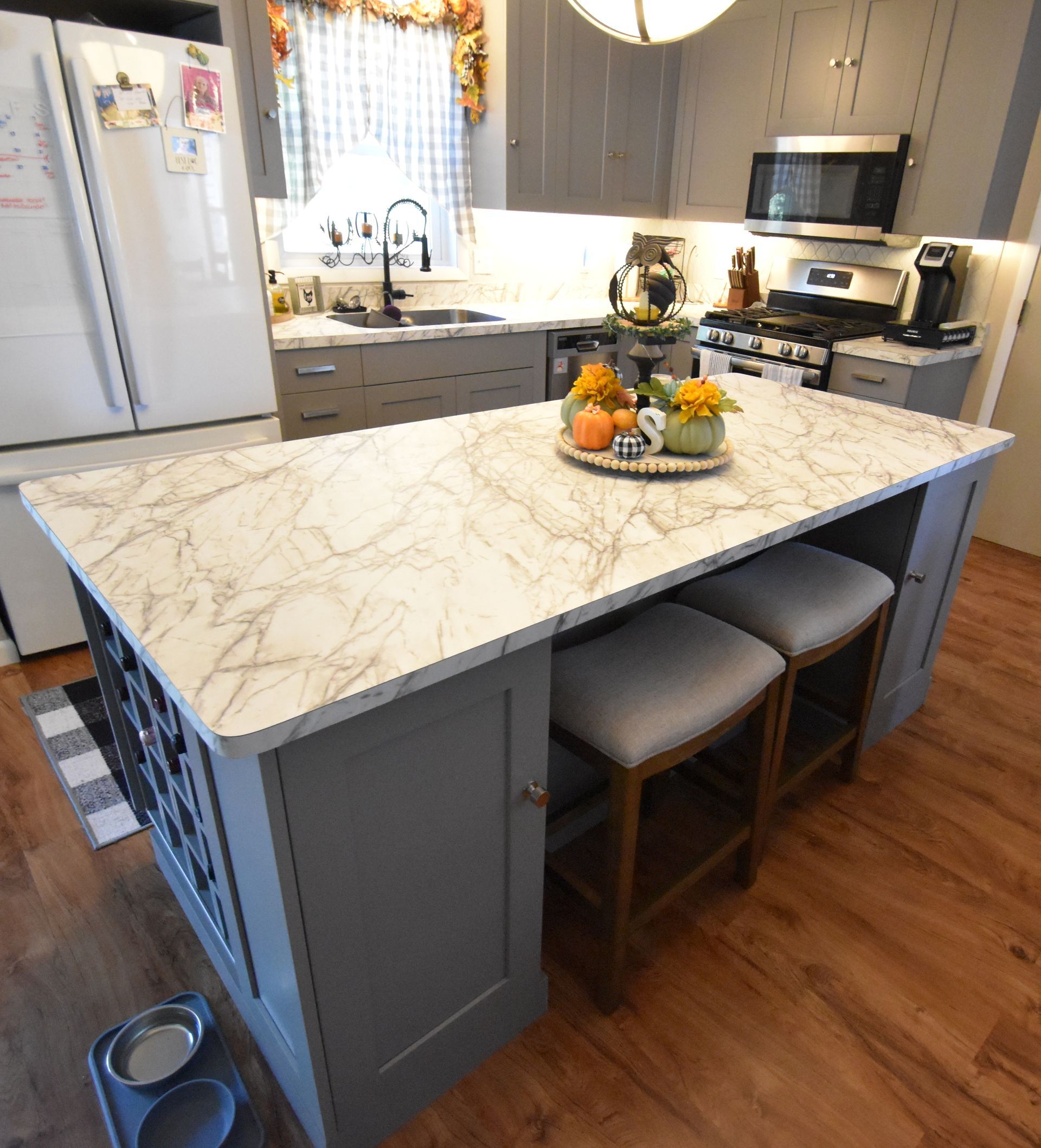 Modern kitchen with large marble island, gray cabinets, stainless appliances, and wood floors