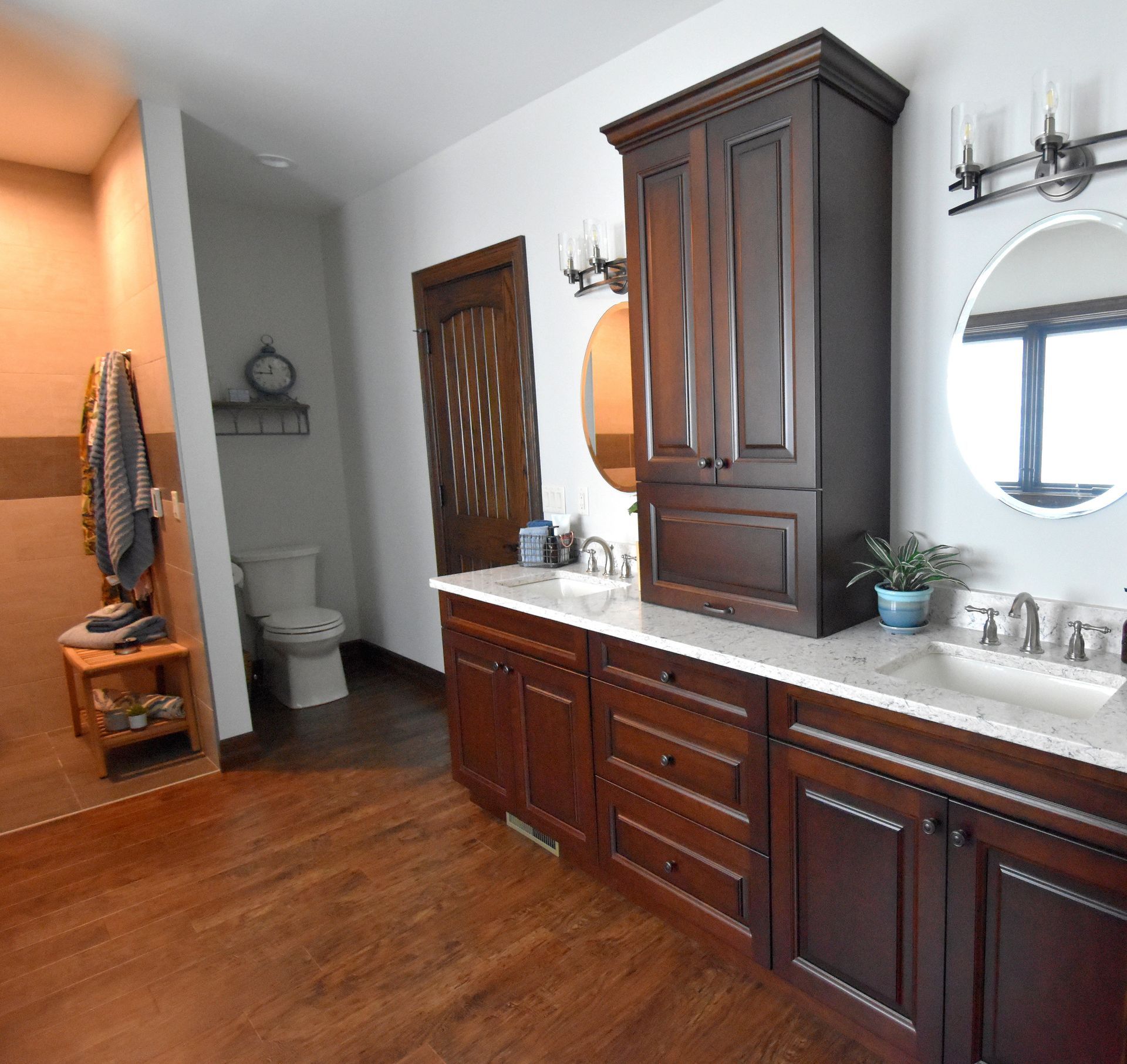 Modern bathroom with dark wood cabinets, double vanity, large mirror, and warm wood flooring