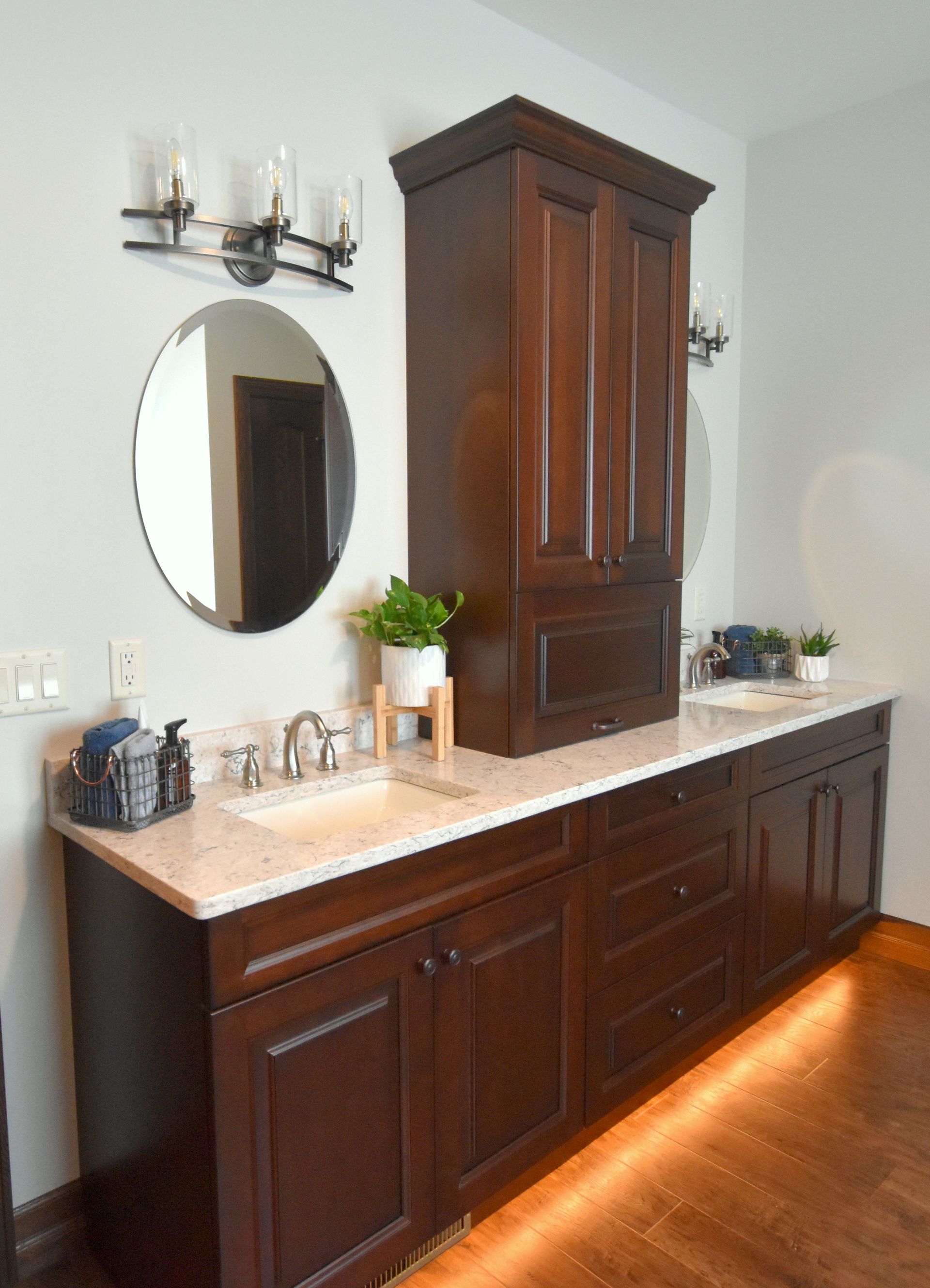 Dark wood bathroom vanity with marble countertop, oval mirror, and wall sconces in a bright room