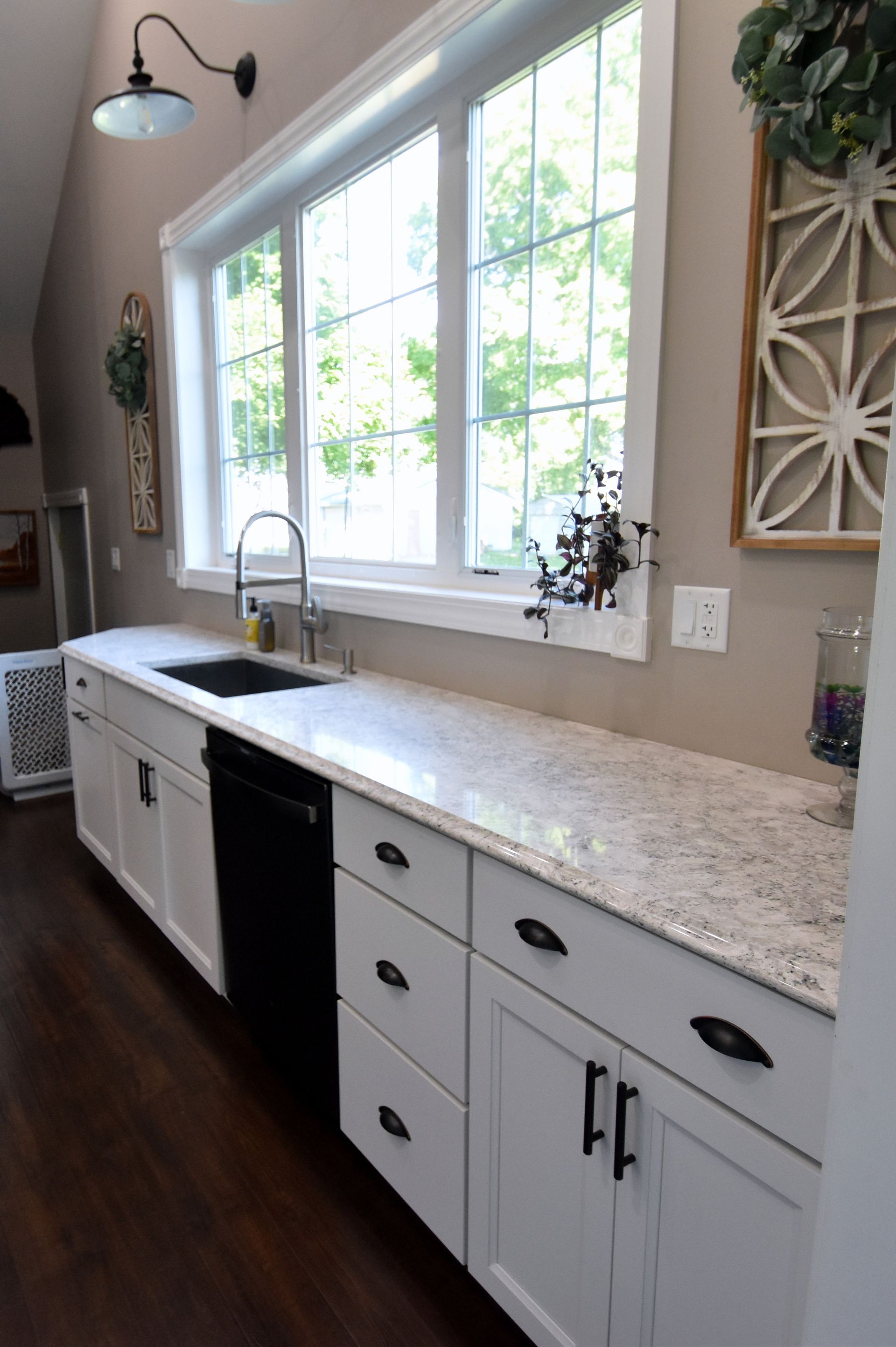 Bright kitchen with white cabinets, stone countertop, sink, and large sunlit windows.