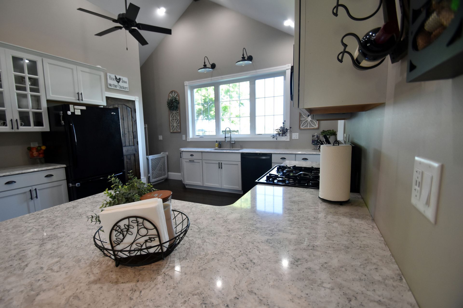 Bright modern kitchen with granite island, white cabinets, black appliances, and window over the sink
