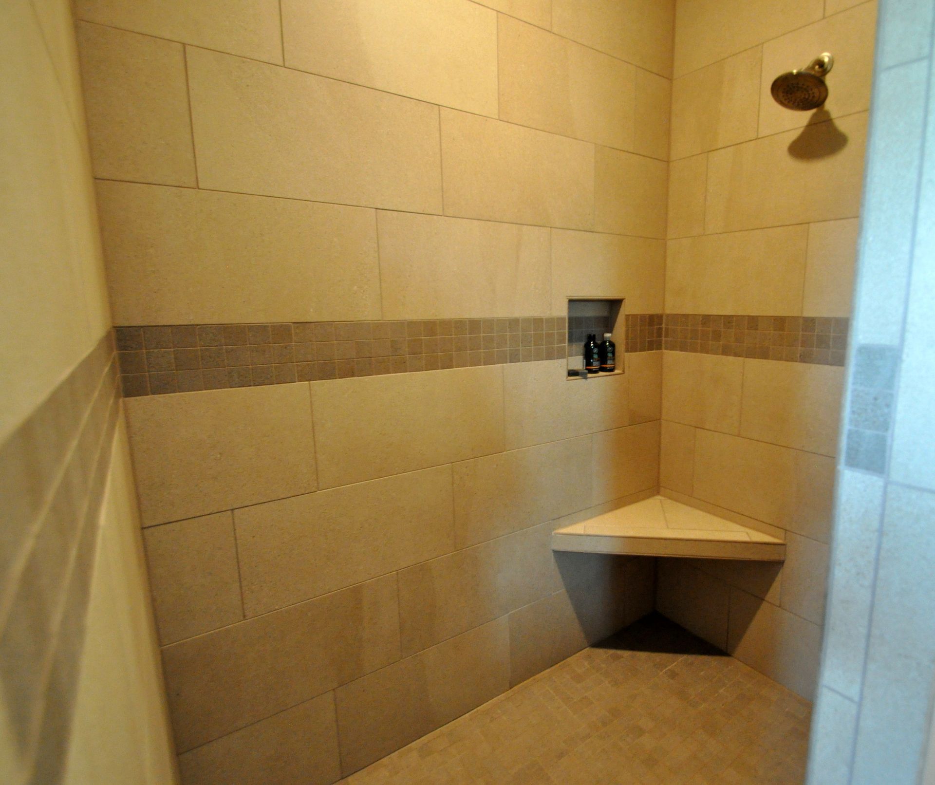 Empty beige tiled shower corner with built-in triangular bench and wall-mounted fixture