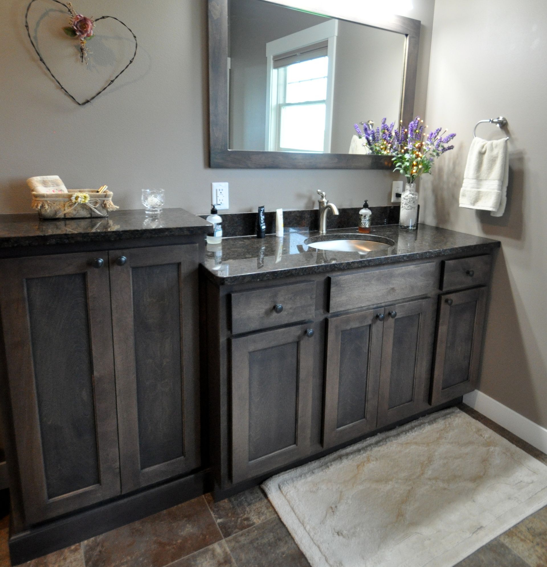 Dark wood bathroom vanity with black countertop, mirror, sink, towel, and white rug.