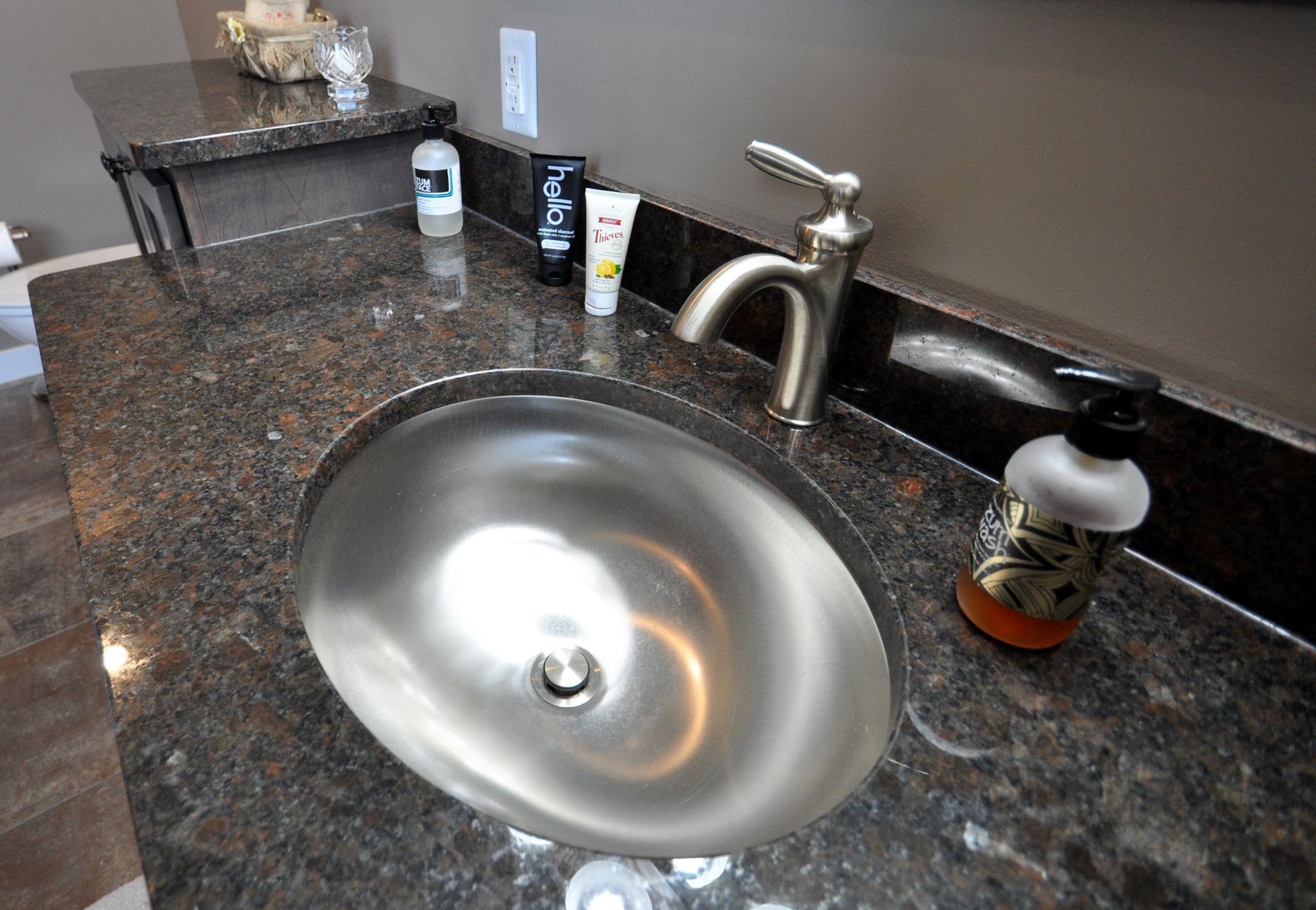 Bathroom countertop with a shiny sink, faucet, soap dispenser, and small toiletries on dark granite.