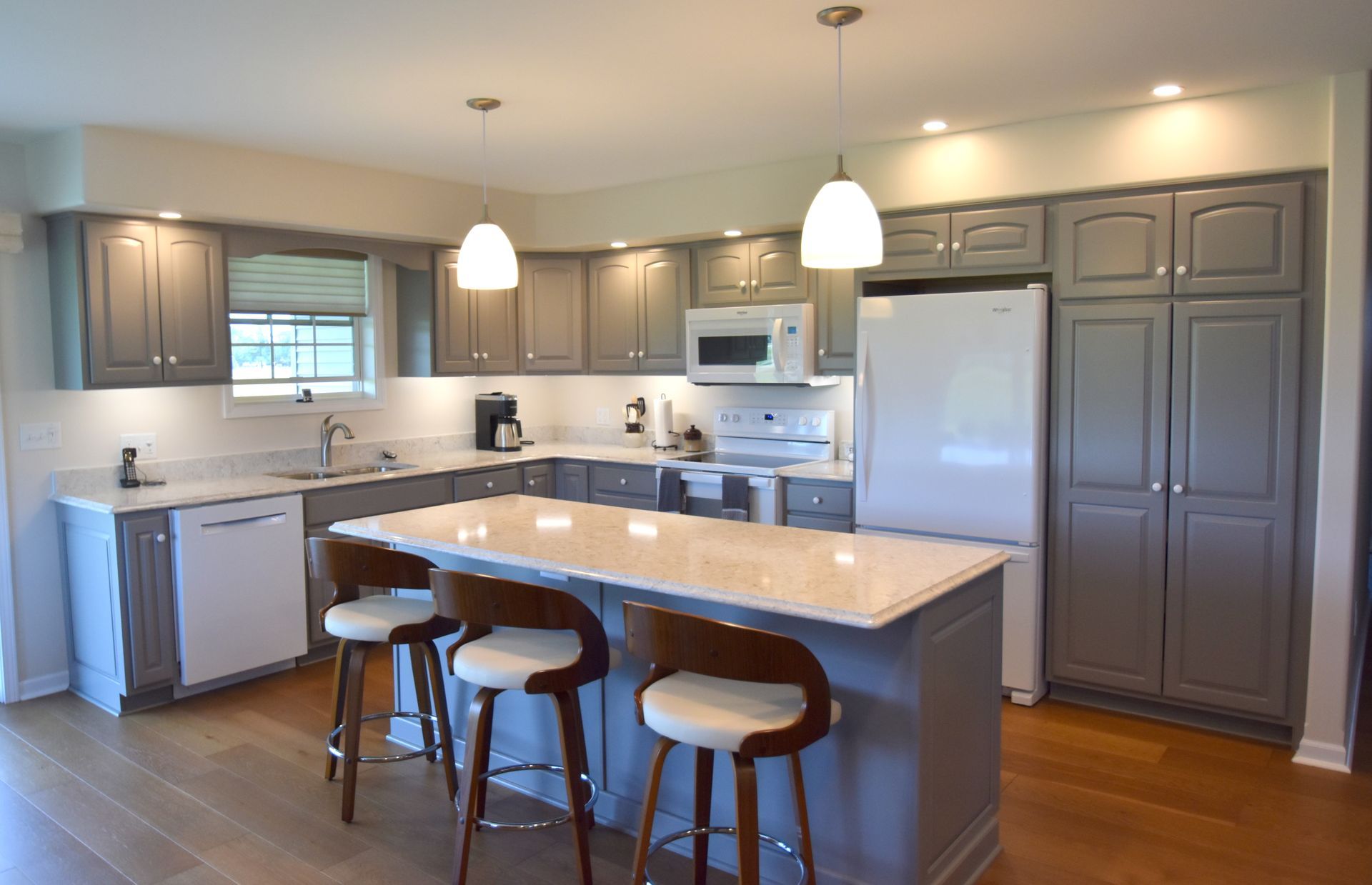 Modern kitchen with gray cabinets, white island, bar stools, pendant lights, and stainless steel appliances