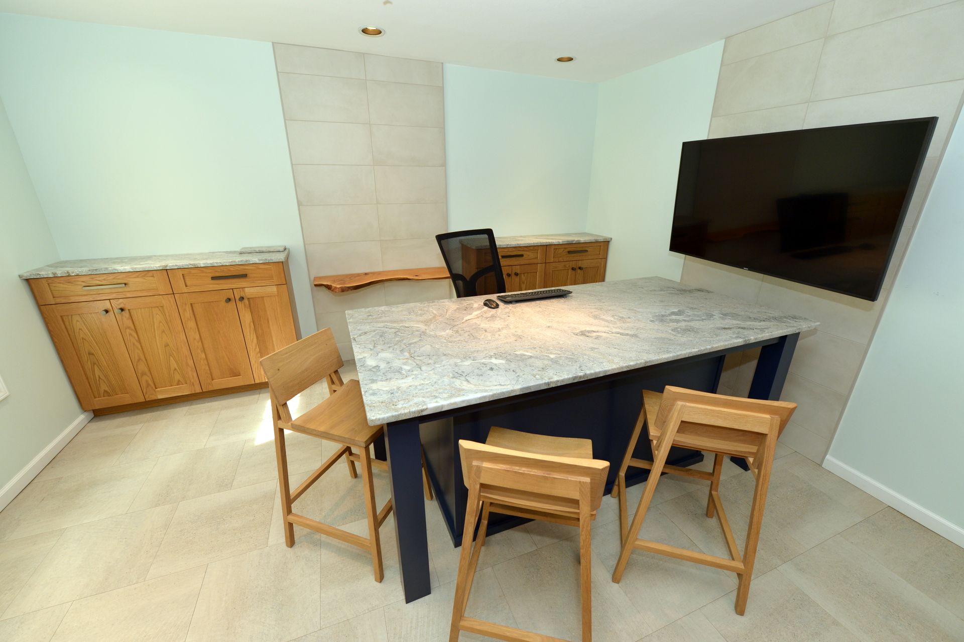 Modern kitchen with granite island, wooden stools, cabinets, and wall-mounted TV.
