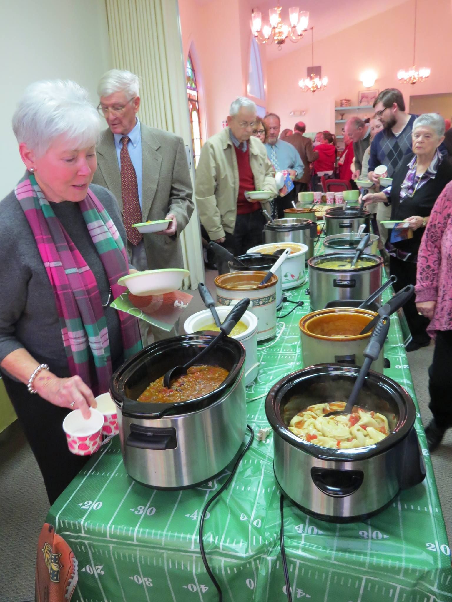 A group of people are standing around a table filled with crock pots of food.