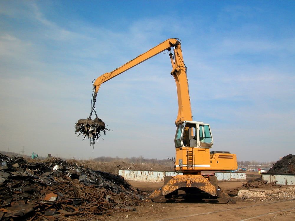 A Yellow Excavator Is Loading Metal Into A Pile Of Scrap Metal — Caloundra Scrap Metal in Landsborough, QLD