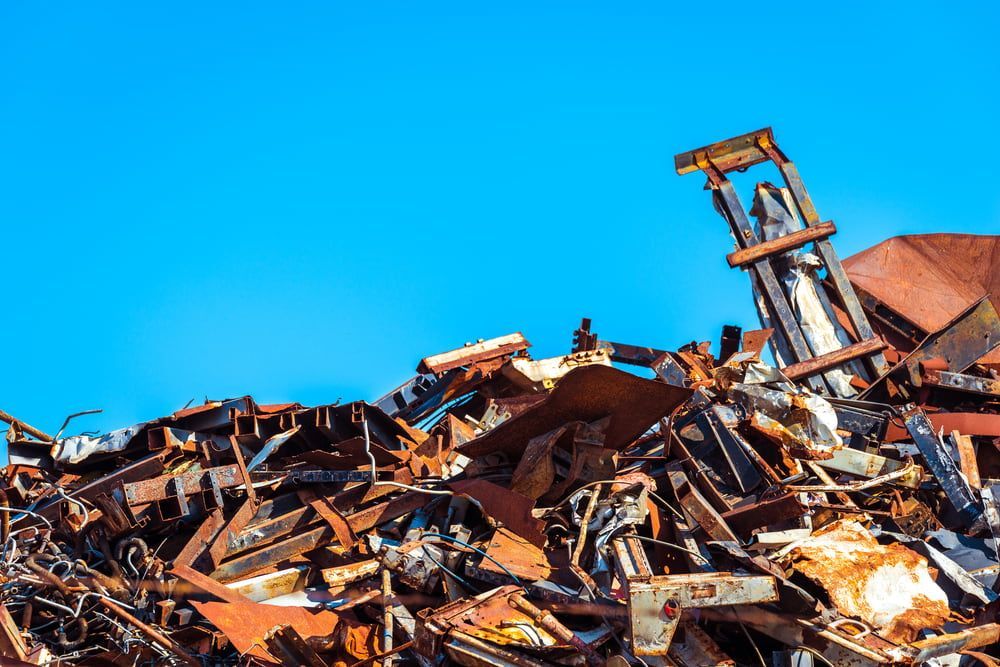 A Pile Of Scrap Metal Against A Blue Sky With A Forklift — Caloundra Scrap Metal in Landsborough, QLD