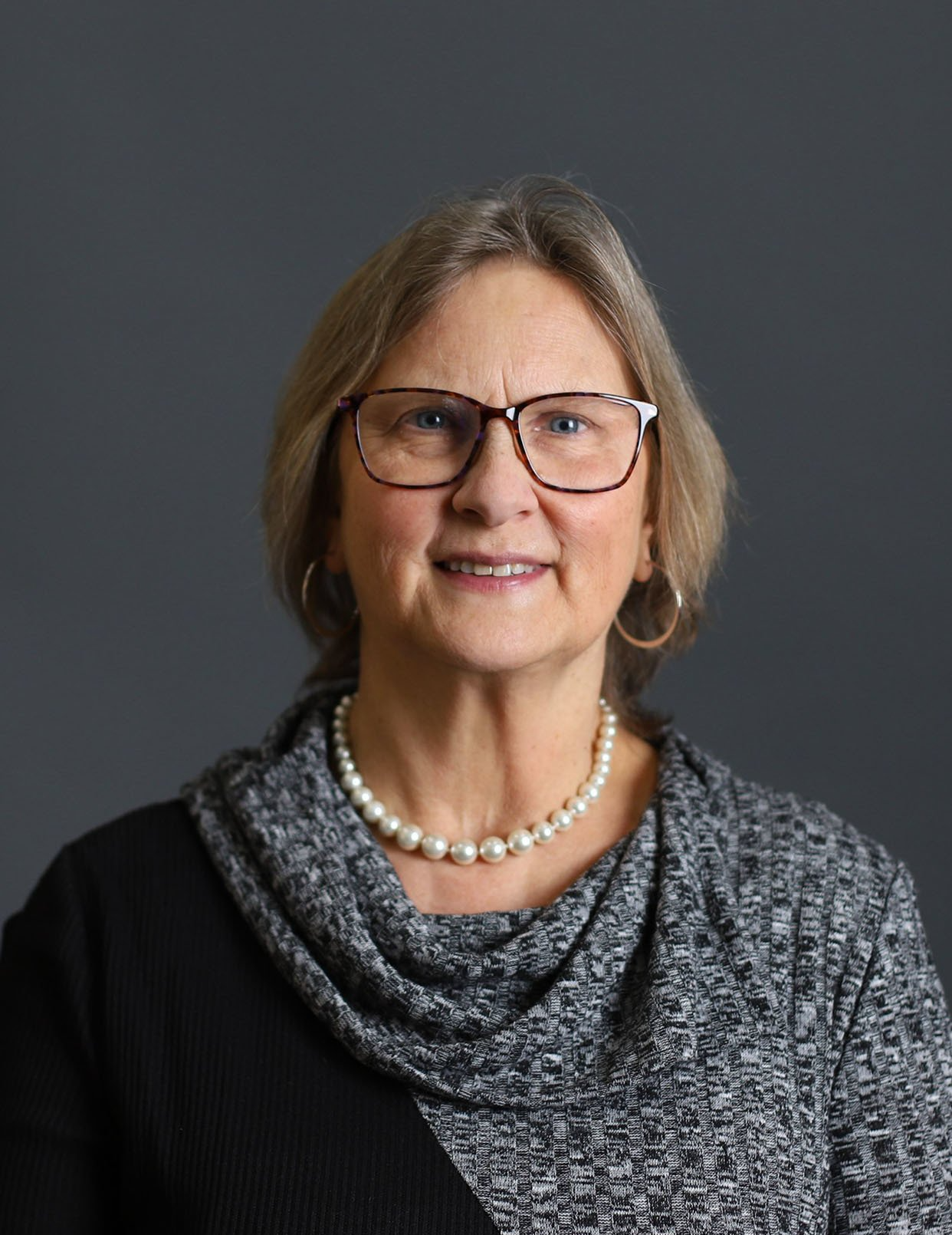 A woman wearing glasses and a pearl necklace is smiling for the camera.