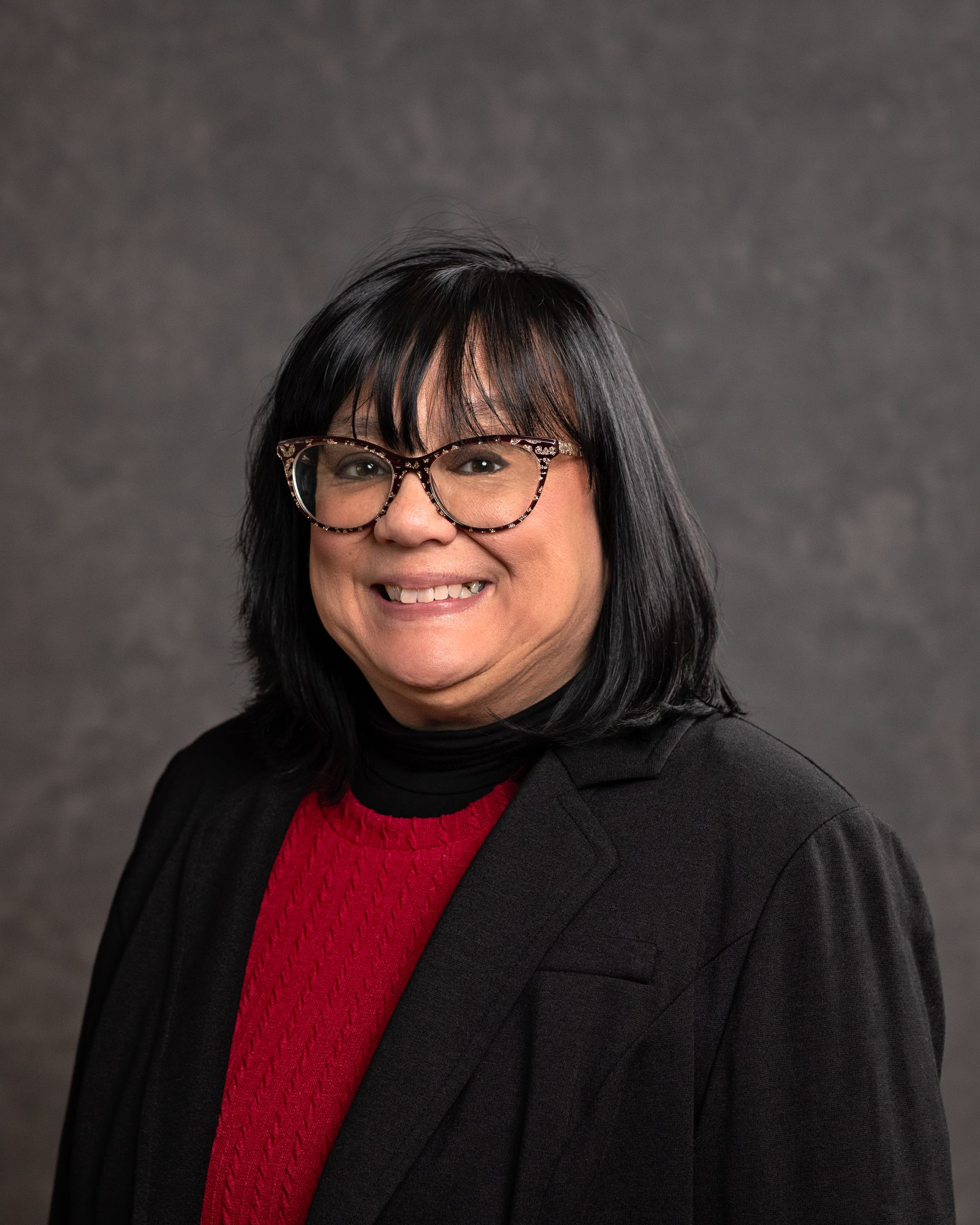 A woman wearing glasses and a red sweater is smiling for the camera.