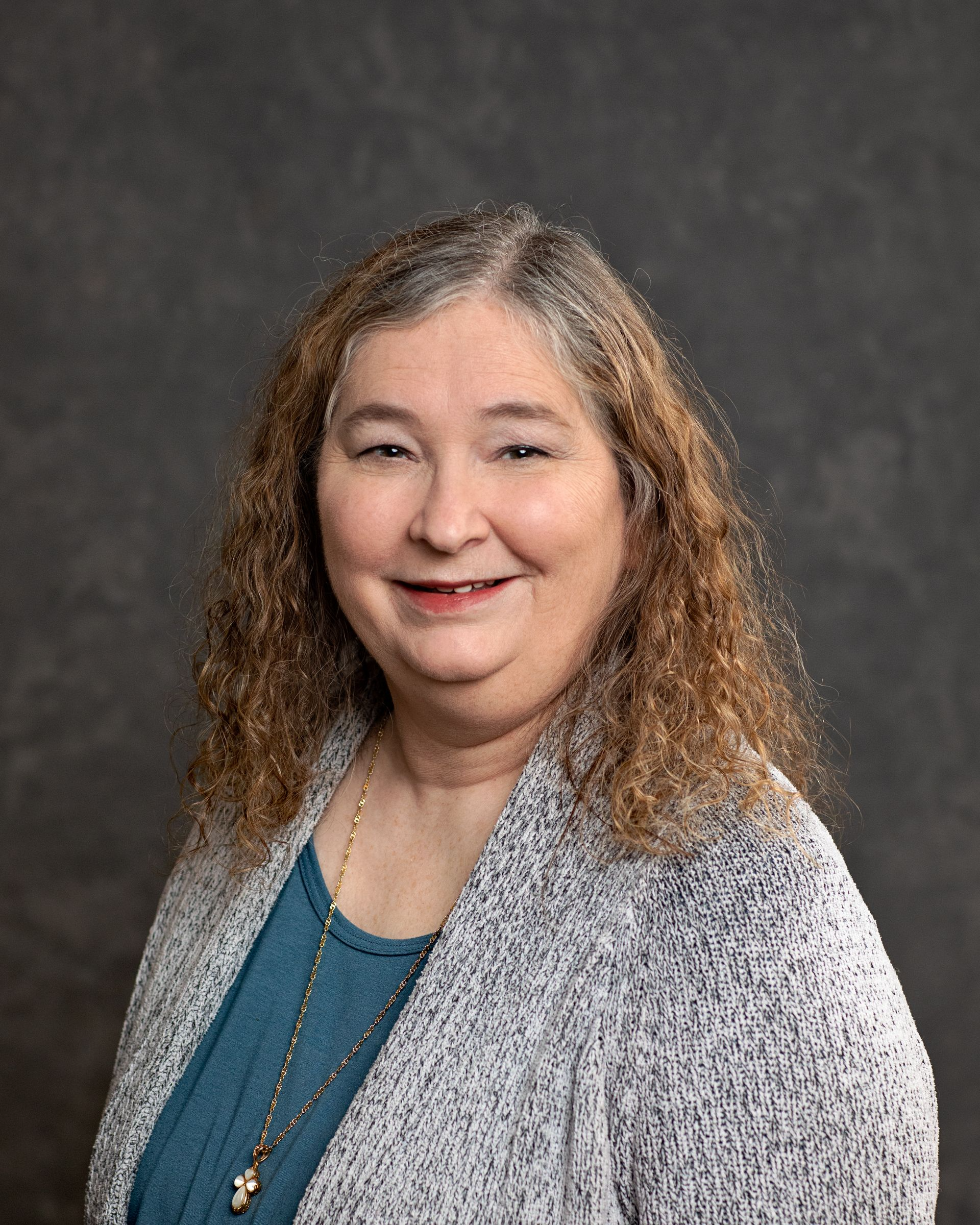 A woman wearing a gray sweater and a blue shirt is smiling for the camera.