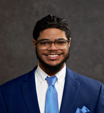 A man wearing a blue suit and tie is smiling for the camera.