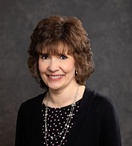 A woman wearing a black sweater and a polka dot top smiles for the camera