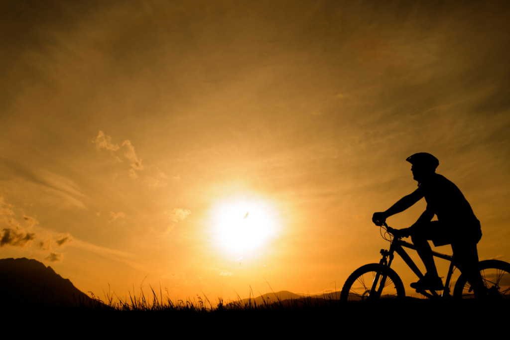 A silhouette of a person riding a bike at sunset.
