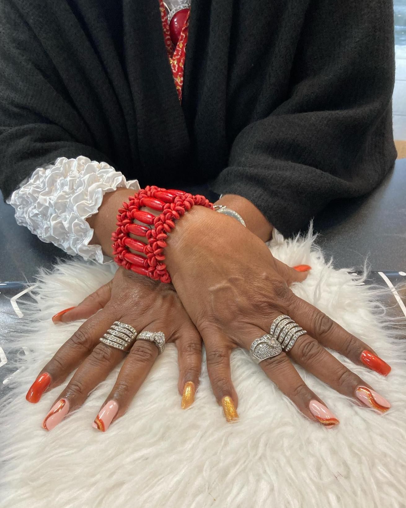 Hands with manicured nails, rings, and a red beaded bracelet. 