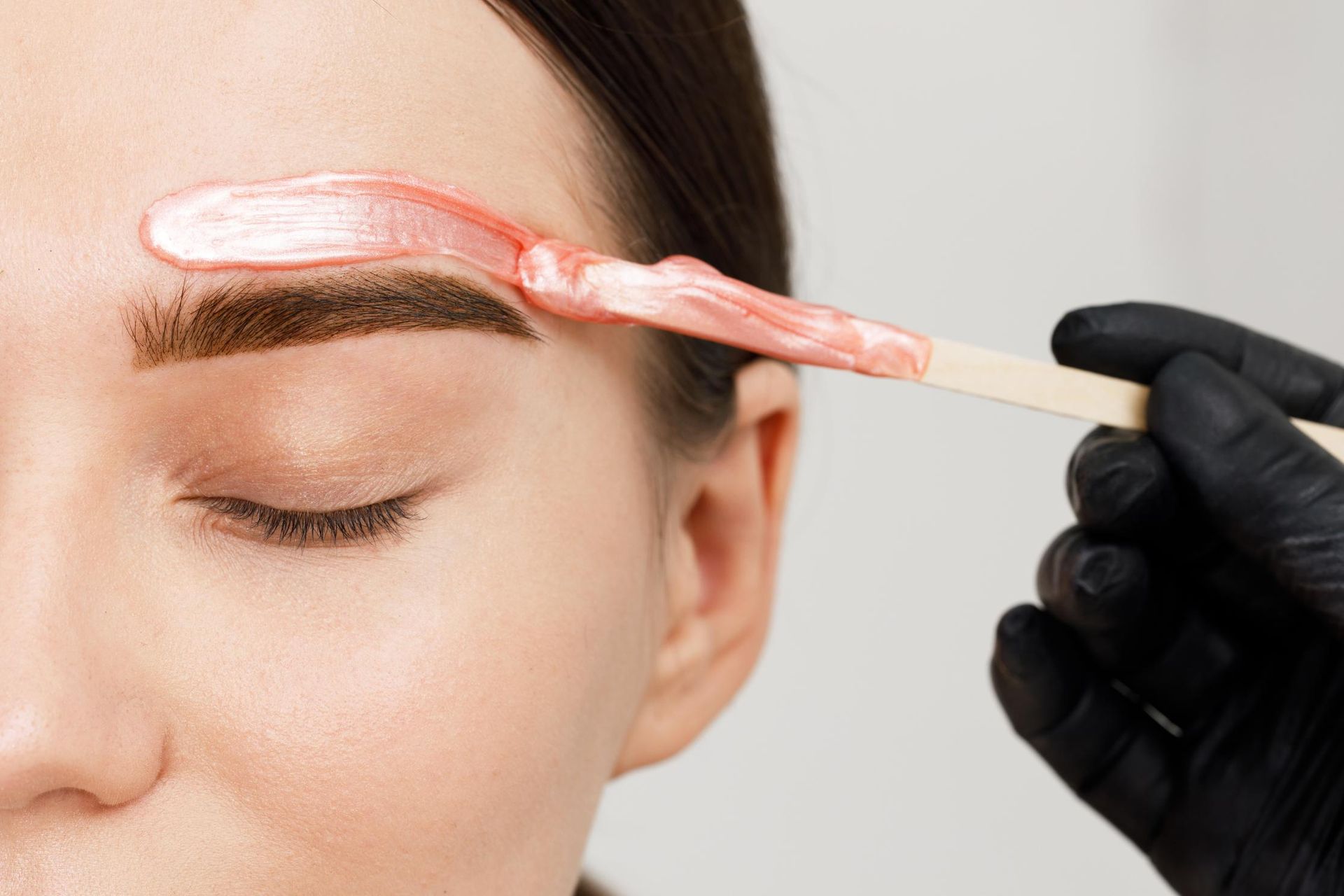 Applying pink wax to shape eyebrow. 