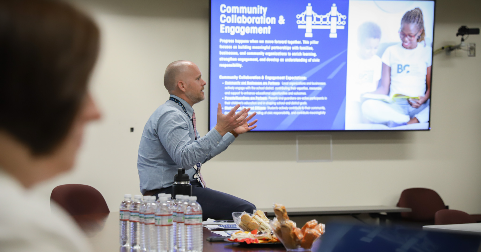 District leader presenting a Community Collaboration and Engagement strategic plan slide to staff in a conference room.