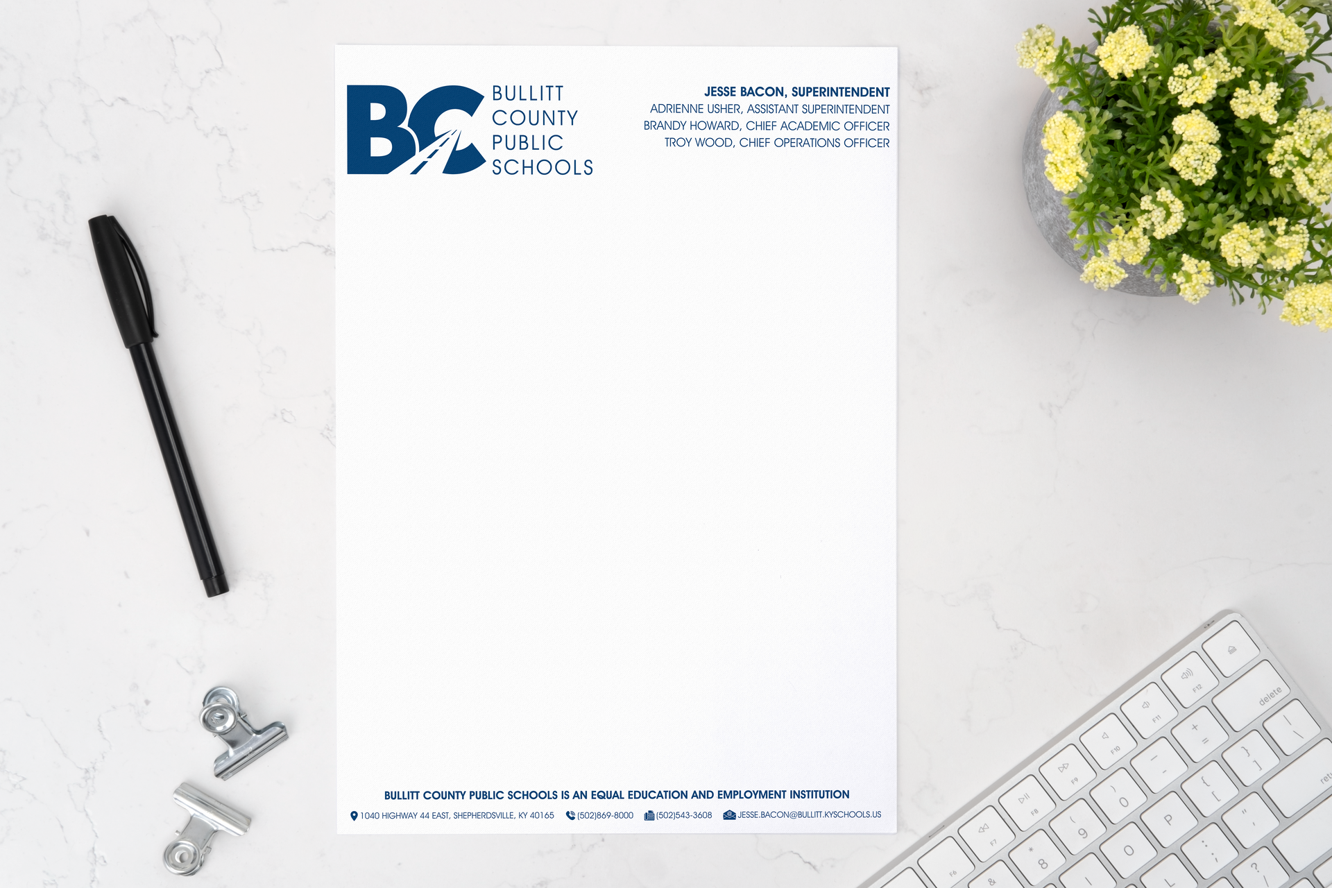 A letterhead is sitting on a desk next to a pen and a keyboard.