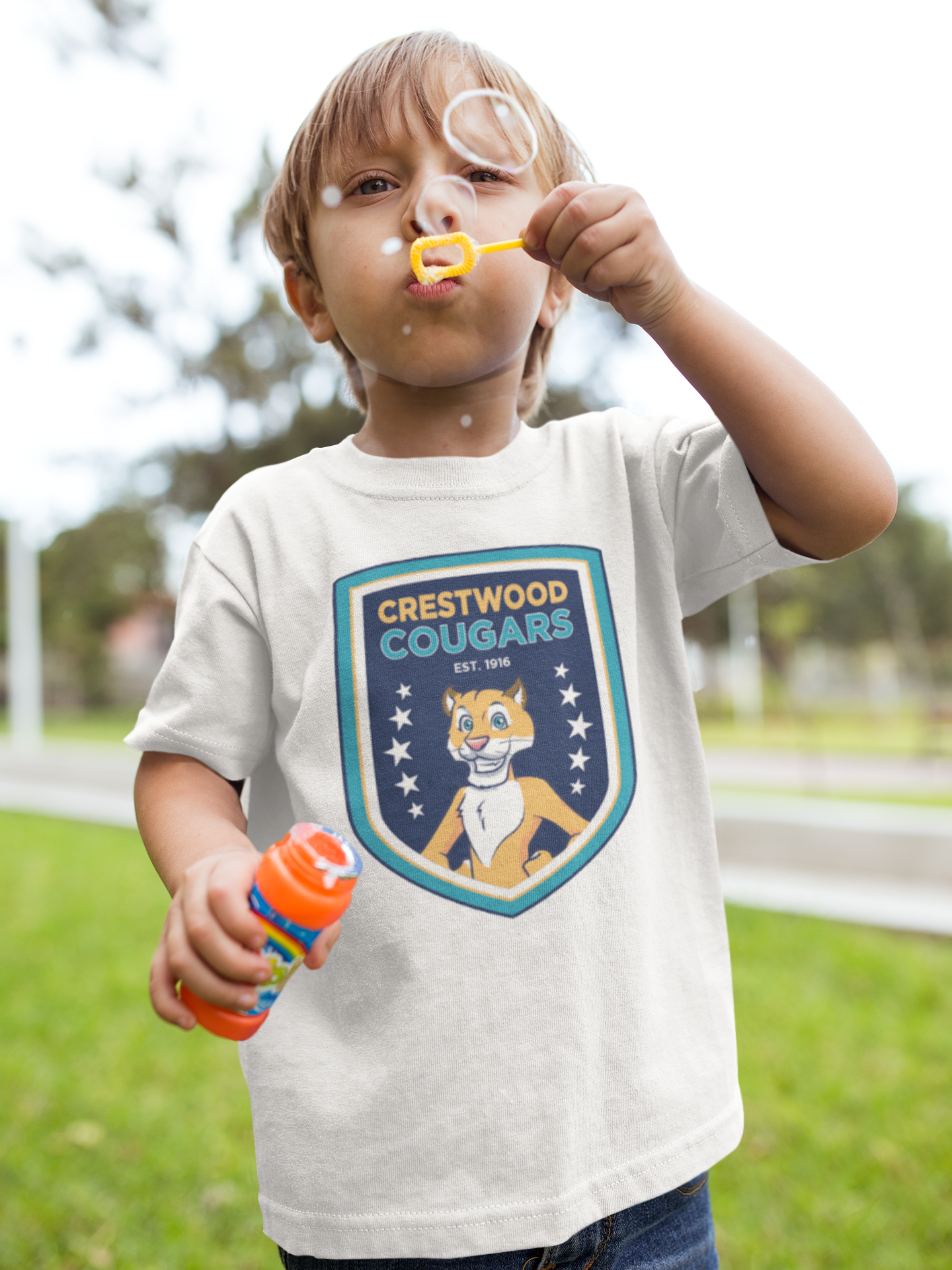 A young boy blows bubbles outdoors while wearing a white t-shirt with the