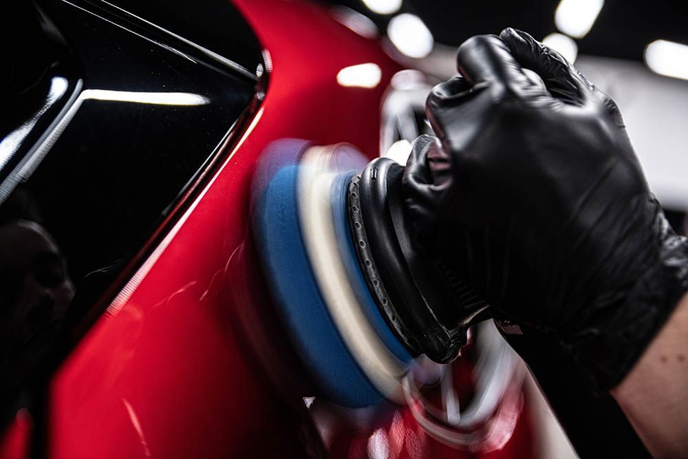 Detail technician applying rotary polisher to red car panel during paint correction.