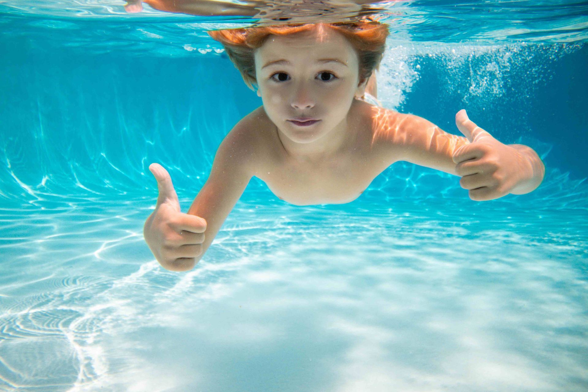 A boy underwater in his pool, swimming with thumbs up