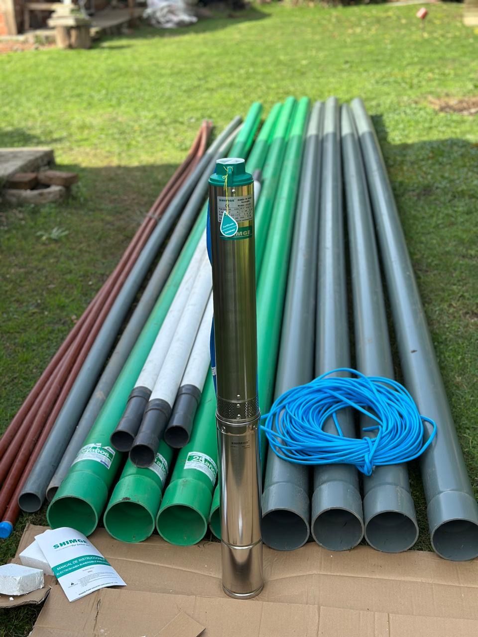 Bomba sumergible con tuberías y cable eléctrico sobre césped.