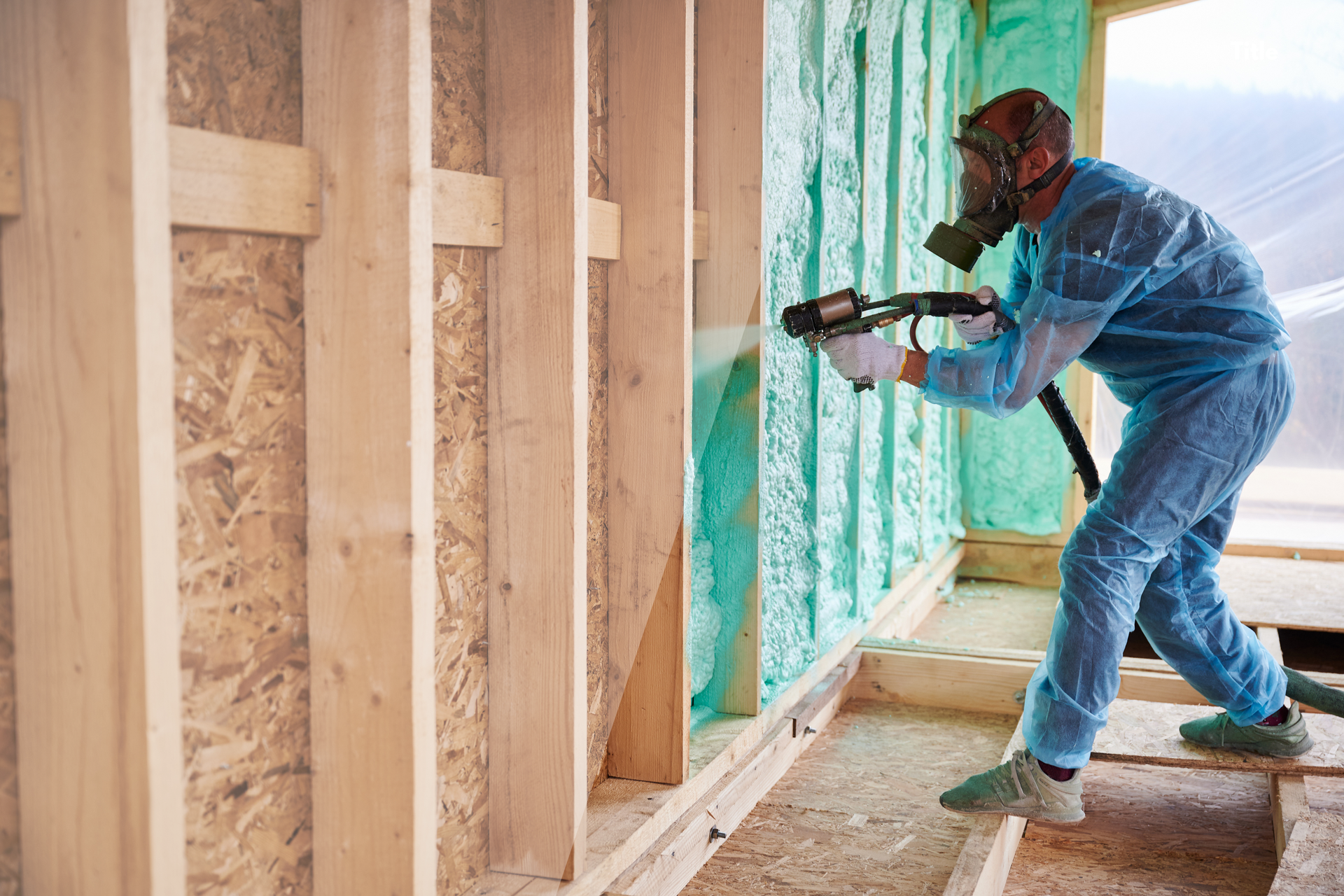 Worker in blue coveralls drilling into a wall frame during home construction