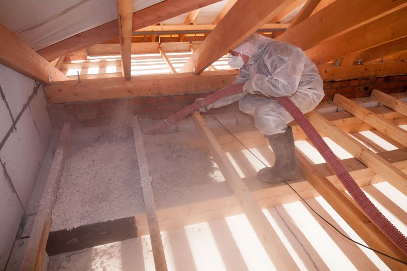 Person in protective suit spraying insulation into attic.