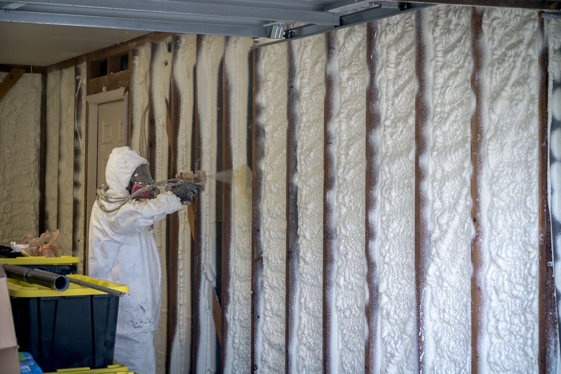 Person in protective suit spraying insulation foam onto a wooden wall.