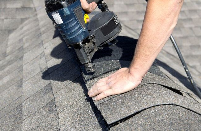 Worker repairing a roof on a white house under a clear blue sky