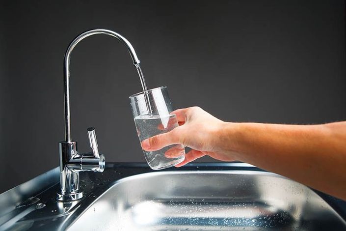 Hand filling a clear glass with water from a kitchen faucet over a stainless-steel sink